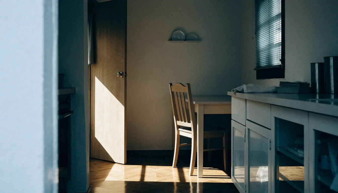 A calm kitchen at midday with window light on the floorboards and nothing on the table